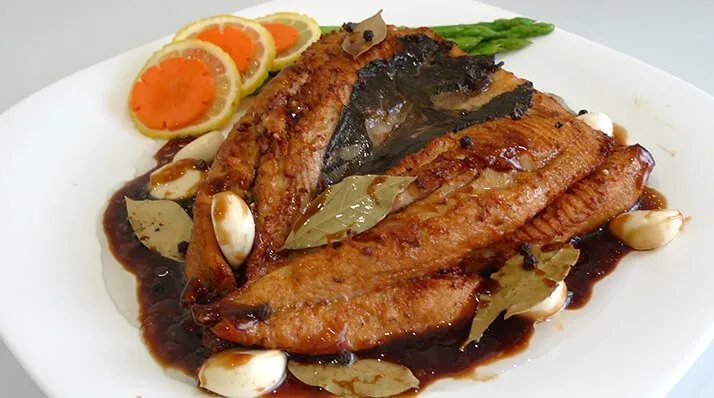 Bangus adobo with garlic and bay leaves on a white plate