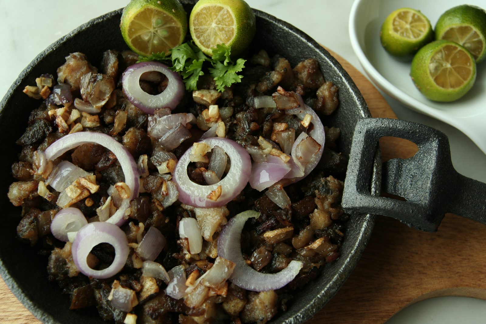 Milkfish sisig with onions in a cast-iron skillet, with calamansi on the side
