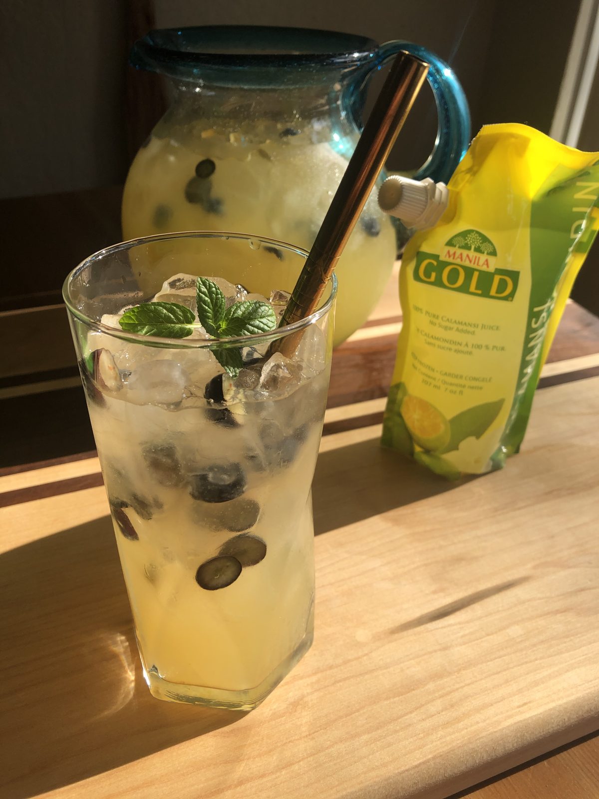 A glass and pitcher of calamansi-ade beside Manila Gold Pure Calamansi