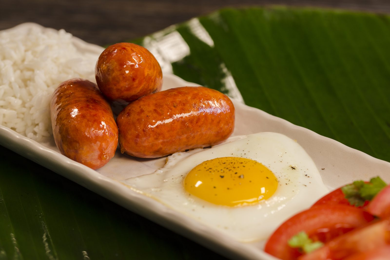 Longanisa sausages with a fried egg, garlic rice and tomatoes on a banana leaf