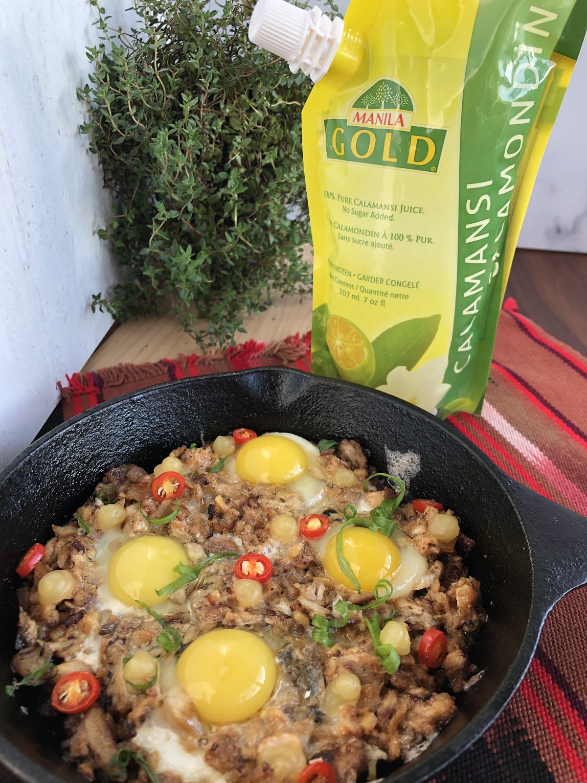 Milkfish sisig with eggs in a cast-iron skillet, next to Manila Gold Pure Calamansi