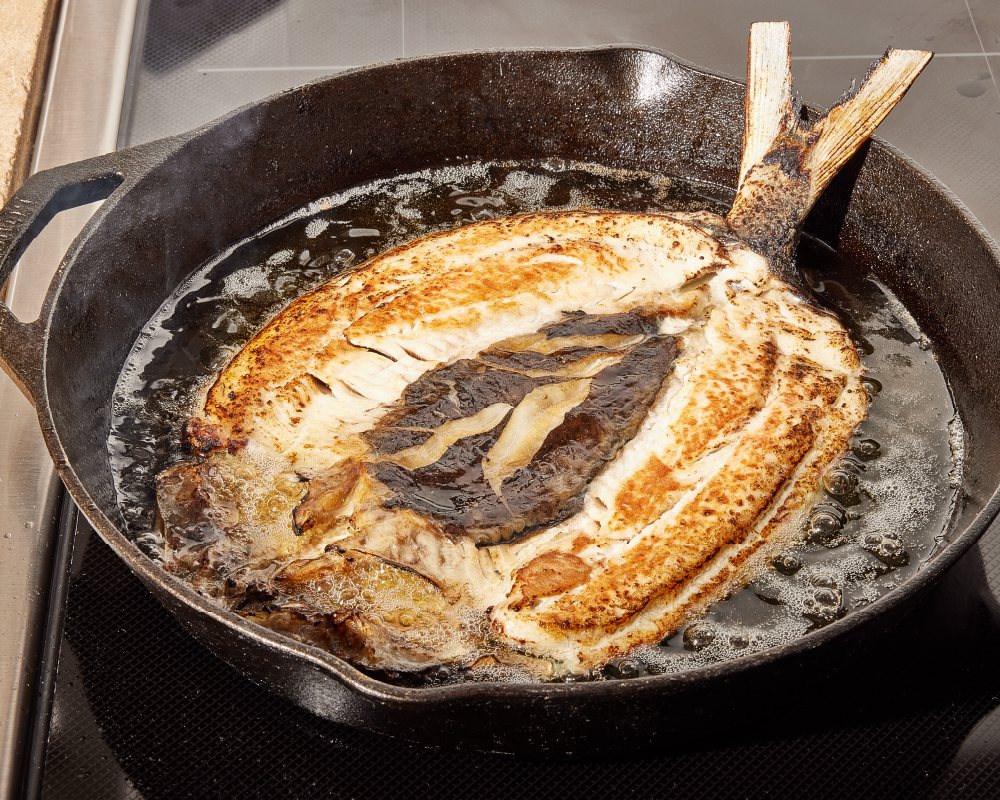 Butterflied bangus searing in a cast-iron skillet