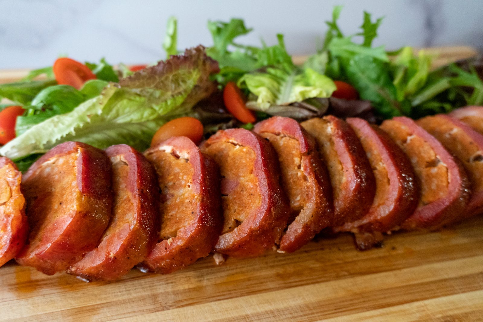 Sliced tocilong roulade on a board with salad greens and tomatoes